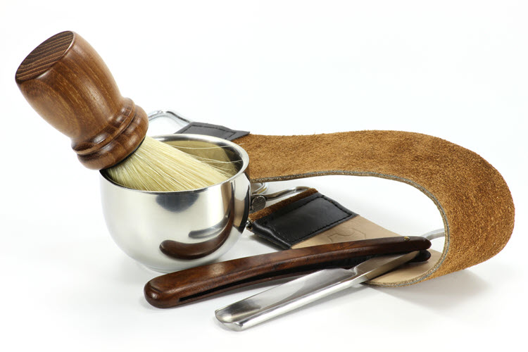 A straight razor, strop, shaving brush and bowl on a white background