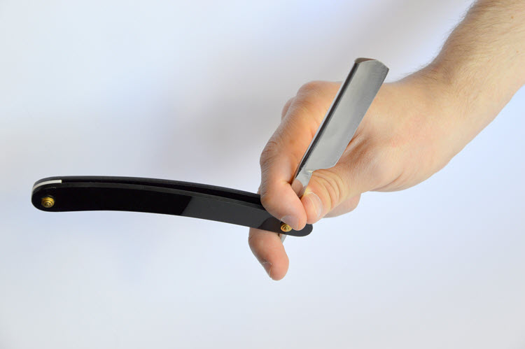 A male hand holding a black-handled straight razor on a white backgound