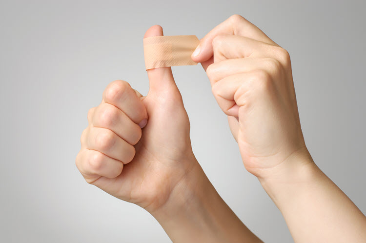 A picture of a woman putting a band-aid on her right thumb. Only the woman's hands are showing.