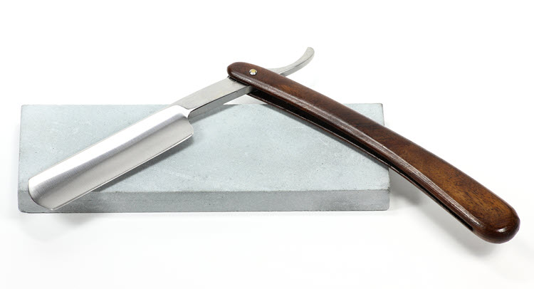 A straight razor on top of a sharpening stone
