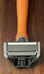 An image of a Harry's razor cartridge resting on a bright orange handle.