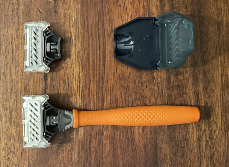 A picture showing a Harry's razor with bright orange handle, protective case and a spare cartridge razor.