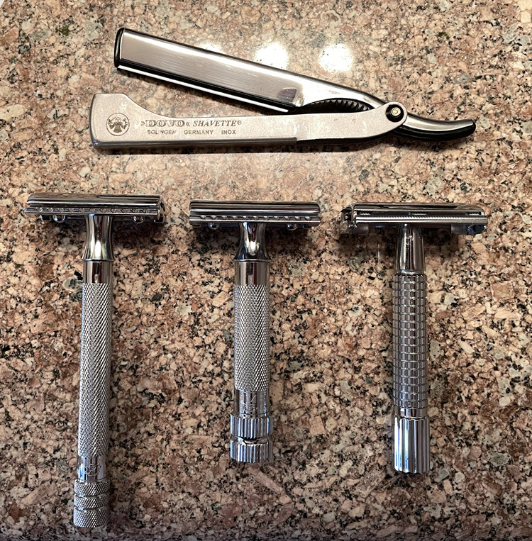 Dovo shavette above three safety razors on a bathroom sink countertop.